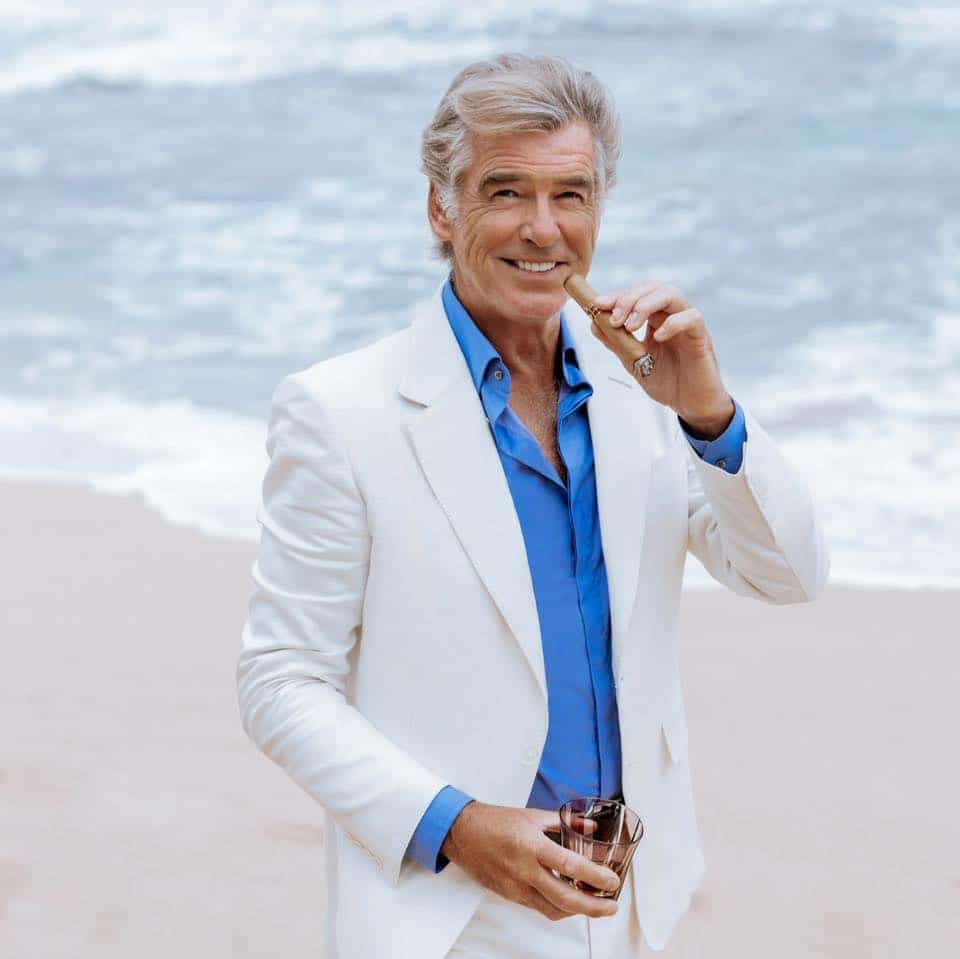 Pierce Brosnan smoking a cigar on shore